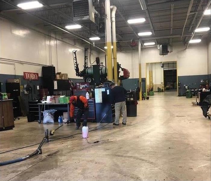 A warehouse with multiple stations that have workbenches and tool boxes. Floors are being cleaned by SERVPRO professionals.