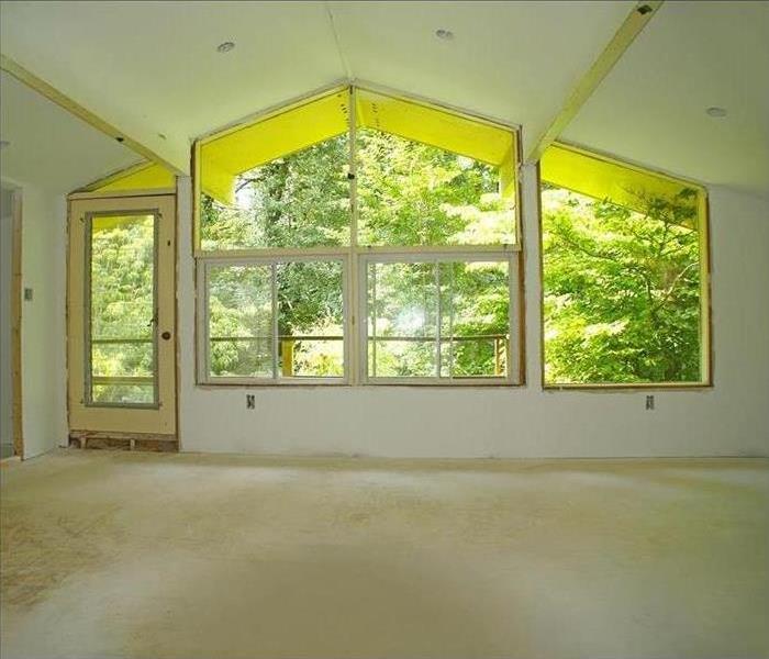A large master bedroom with many windows facing the back woods with a deck. Bare floors and fresh drywall ready to renovate.