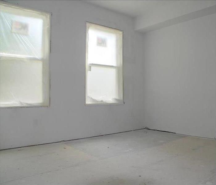 An empty bedroom with two new windows, fresh drywall, and bare floors.