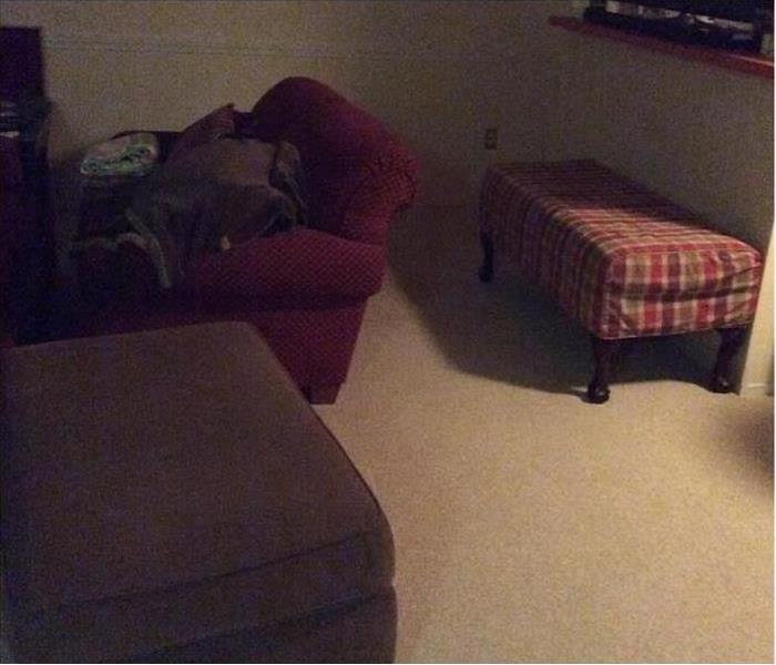  A finished basement room with chairs and ottomans and the carpet is wet. 