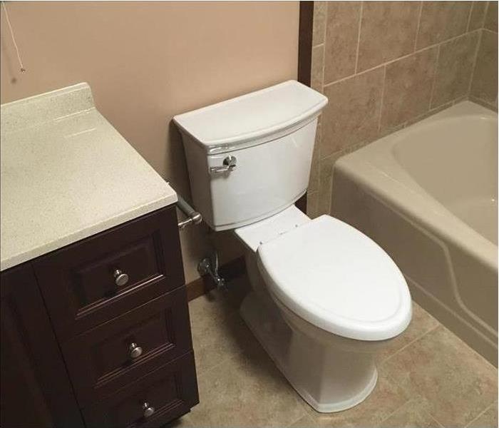 A complete remodel of the bathroom showing new toilet, floors, tub, and sink.