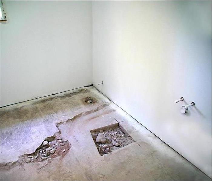 A small empty bathroom; the floor gutted down to the cement, fresh drywall, and new pipes ready for a sink and toilet.