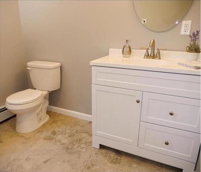 A finely finished small bathroom with new flooring, baseboards, toilet, sink with cabinets, and a mirror.