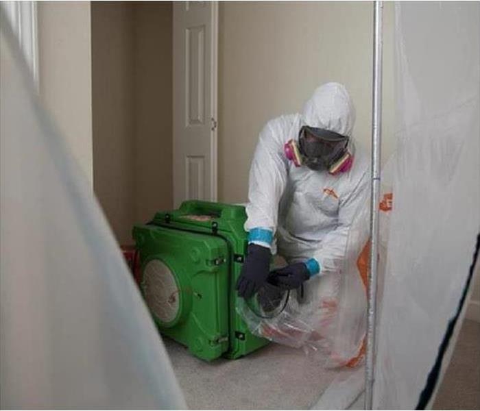 A worker wearing a protective mask and clothing cleans up mold.