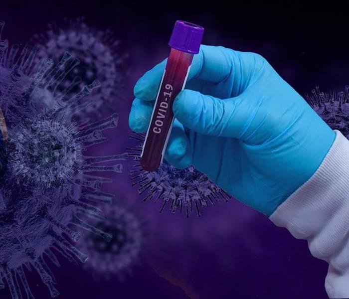 A blood sample held by a gloved hand in front of a background of a virus image